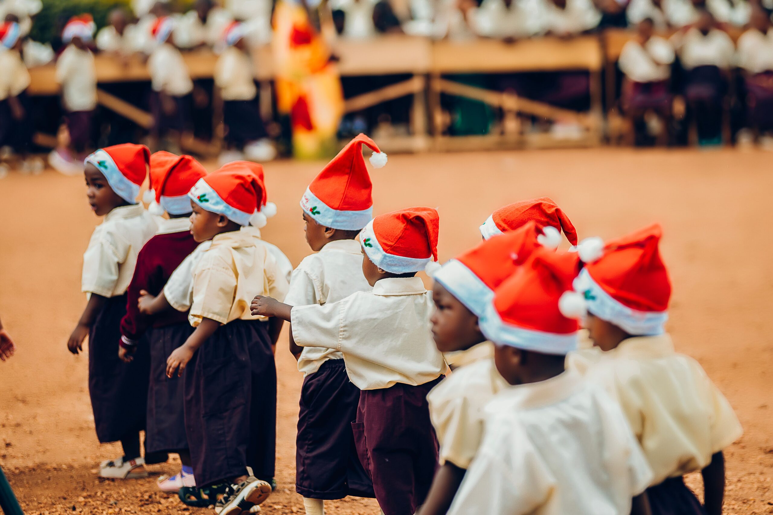 A group of children wearing Santa hats participate in an outdoor festivity, spreading holiday cheer.